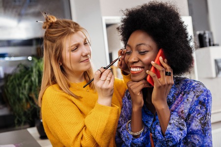 Good news beautiful smiling african american model with coral lipstick feeling pleased while sitting in a fashion studio Stock Photo