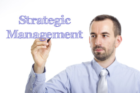 Strategic management young businessman writing blue text on transparent surface horizontal image