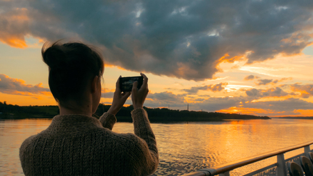 Woman silhouette taking photo of beautiful sunset with smartphone on deck of cruise ship sunset light golden hour photography nature and journey concept