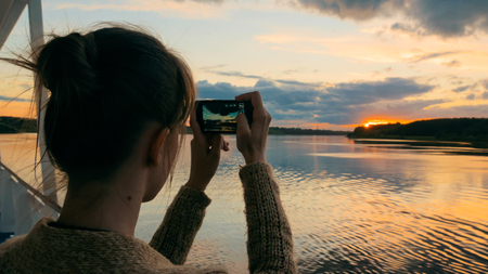 Woman silhouette taking photo of beautiful sunset with smartphone on deck of cruise ship sunset light golden hour photography nature and journey concept