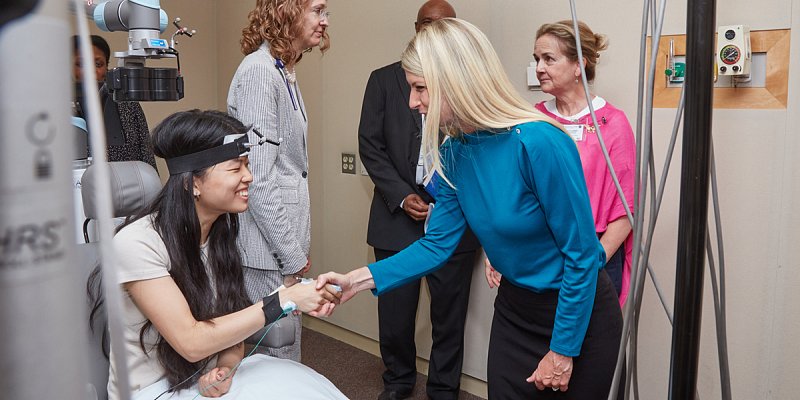 Rep. Brittany Pettersen (right) thanks Pei Robins, an Intramural Research Training Award (IRTA) trainee after a demonstration of transcranial magnetic stimulation (TMS) therapy in the Clinical Center. Dr. Sarah (Holly)  Lisanby, head of NIMH’s noninvasive neuromodulation unit, converses with Rep. Madeleine Dean in the background.