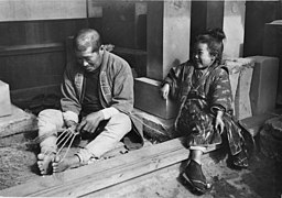 Zori were traditionally made in the home, as were waraji. Note twine warp, held between hands and toes, and loose-fiber weft, to his right.