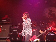 Jeff Keith, lead singer, on stage with Tesla. Guitar player, speakers and drums are in the background.