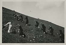 Photographie en noir et blanc d'écolières gravissant une colline verte assez pentue.