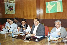 Four men at a table with microphones, water bottles and documents.