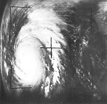 Black and white satellite image of a well-defined tropical cyclone at center left with sprawling rainbands. Due to the angle of the photo taken, the limb of the Earth is visible at far left.