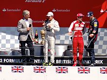 Damon Hill on a stage interviewing three drivers