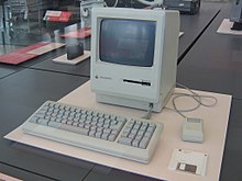 Macintosh Plus monitor, keyboard, mouse, and floppy disk in a museum display case
