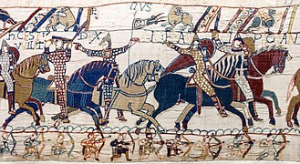 Embroidery depicting 5 armed knights riding in line. Scene 55 from the Bayeux tapestry. Eustache II de Boulogne (whose name, Eustacius, seems to be partially indicated) holds a banner with balls.