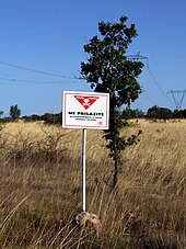 A white painted rectangular warning sign on a metal pole