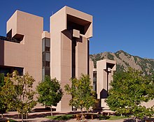 A series of brown boxlike buildings stand in front of a mountain.