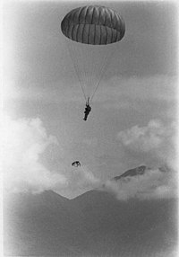 A parachuting marine, descending with an attached dog at a lower elevation