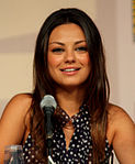 A woman with long brown hair, smiling into a microphone.