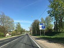 Route avec un panneau de direction bleu sur le côté, indiquant tout droit pour Pskov et tourner à droite pour Ostrov.