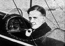 Picture of a man with short hair, sitting in an aircraft cockpit, looking at the camera over his left shoulder.