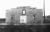 The front of a brick building with white double doors and windows on either side and a sign above the door