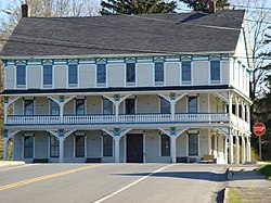 A three-story white building with a full-length second-story balcony, blue trim and a black roof