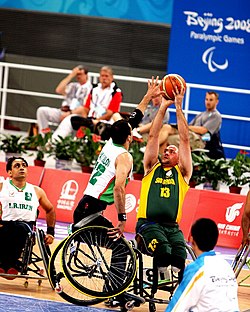 Um atleta tenta arremessar uma bola, enquanto um adversário estica o braço, tentando interceptá-la.