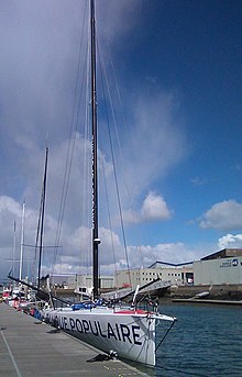 De trois quarts face, un bateau blanc amarré au ponton. « Banque populaire » est écrit en grandes lettres bleues sur la coque.