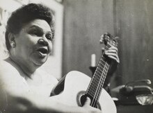 Black and white photograph of a woman singing and playing guitar.