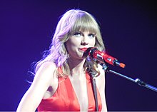 Taylor Swift in a red dress with a microphone near her face.