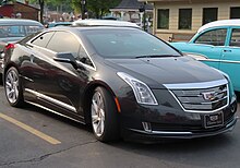 Front three-quarters view of a black 2-door coupe. Featuring a Cadillac badge, vertically-shaped headlights adorn its exterior. It has large wheels, and its license plate says Cadillac ELR, with the former word in an unusual font.