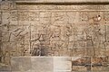 King Taharqa and the gods of Thebes. Standing on the left, he offers "a white loaf" to his father Amun-Re, who is accompanied by Mut, Khonsu and Montu, Kawa shrine.[62]