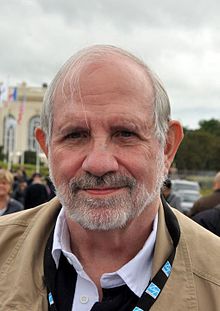 Plan poitrine d’un homme de 67 ans, barbe blanche, moustache grise, front dégarni, regard droit vers l'objectif, léger sourire.