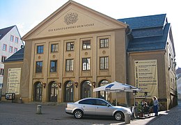 Barevná fotografie s pohledem na trojosé průčelí divadelní budovy, uprostřed je trojúhelníkový štít