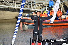 De face, debout à l'avant son bateau, souriant, les deux bras levés, il salue la foule dans le chenal des Sables-d'Olonne.