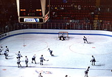 Vue d'une partie de la patinoire du Colisée de Québec à partir des gradins. Des joueurs des Nordiques de Québec s'échauffent en tirant tour à tour sur le gardien de but