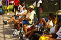 Spectators bring their own chairs and park in the rear. Some wear brims and eyewear for protection from stray balls.