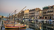 Dans une large voie d'eau citadine des barques colorées s'alignent perpendiculairement à un quai.