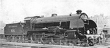 Side-and-front view of a 4-6-0 locomotive on a turntable. A member of the crew is standing next to the front.