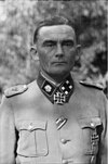 A black-and-white photograph of a man wearing a military uniform and neck order in shape of an Iron Cross. His hair is combed back and his facial expression is determined.