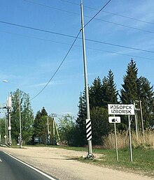 Photographie d'un panneau d'entrée dans un village, ici Izborsk, écrit en russe et en anglais.