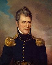 A man with graying, wavy hair wearing a high-collared black military jacket with gold epaulets and buttons