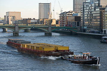 Barges loaded with containers being towed by a tugboat on the River Thames in London, England, UK