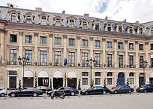 Color photograph of a building, seen slightly in profile, in the classical four-storey style. The facade features chains of refractions on the ground and mezzanine floors, as well as alternating dormers and oculi.