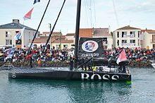 Le bateau avance dans le chenal des Sables-d'Olonne. À l'avant, le navigateur salue la foule.