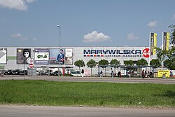 A metal wall of a simple, cuboid building, with mall’s and multiple advertisements