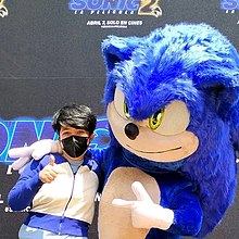 On the right, a Sonic the Hedgehog mascot costume is posing next to a young child wearing a face mask at the Los Angeles premiere of the film.
