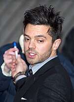 A brunette man stares to his left as he signs autographs