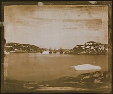 a sepia toned photographic view of four ships in the distance sailing through a channel.