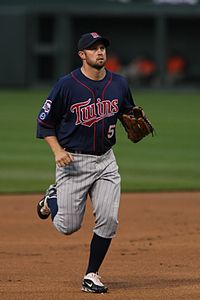 A man in a navy blue baseball jersey and cap and gray pants