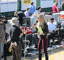 Erin Andrews is seen from a distance holding a microphone as she speaks to a camera