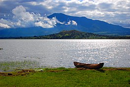 Lake with wooden canoe in foreground, mountain in distance.