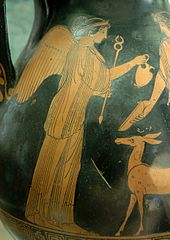 Foto bagian vas hitam dengan gambar coklat di atasnya: Seorang wanita dengan sayap di punggungnya memegang anak panah dengan tangan kanannya dan memberikan toples kepada seorang pria. Seekor rusa kecil berdiri di depan wanita itu.