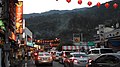 City street with heavy traffic, orange overhead lanterns, and mountains in the background