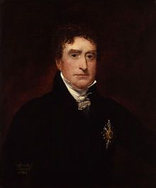 a portrait of a young man with dark hair and dark eyes. He is wearing a black jacket with some form of medal or badge pinned to the front, along with a raised collar and a small cravat.